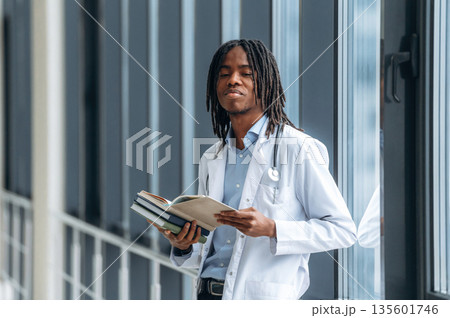Lot of learning material, holding books. Young male black doctor is in the corridor 135601746