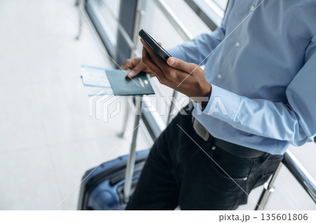 Phone and tickets in hands. Male tourist is in the airport corridor Phone and tickets in hands. Male tourist is in the airport corridor 135601806