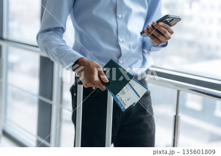 Smartphone and tickets in hands. Male tourist is in the airport corridor 135601809