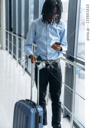 Smartphone and tickets in hands. Male tourist is in the airport corridor Smartphone and tickets in hands. Male tourist is in the airport corridor 135601810