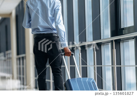 Walking with suitcase. Male tourist is in the airport corridor 135601827