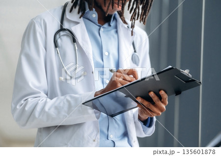 Writing the information into notepad. Close up view of doctor in coat indoors Writing the information into notepad. Close up view of doctor in coat indoors 135601878
