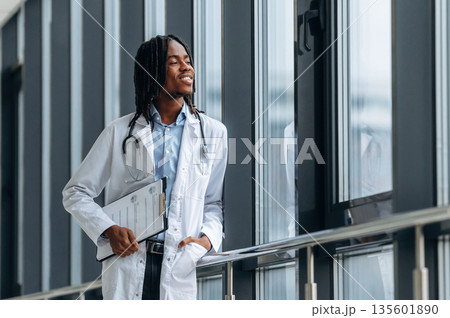 Leaning on the railings near windows. Young male black doctor is in the corridor 135601890