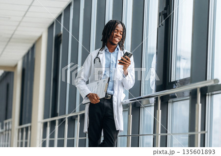 Joyful, positive facial expression. Young male black doctor is in the corridor Joyful, positive facial expression. Young male black doctor is in the corridor 135601893