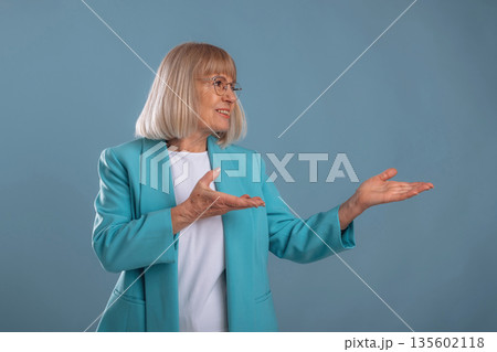 Showing to the side. Senior woman is against background Showing to the side. Senior woman is against background 135602118