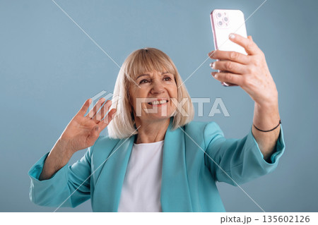 Smartphone in hand, online call. Senior woman is against background 135602126