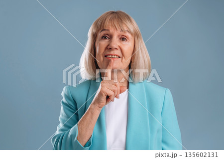 Be silent, finger before the lips. Senior woman is against background Be silent, finger before the lips. Senior woman is against background 135602131