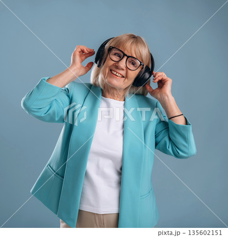 Listening to music, enjoying. Senior woman is against background Listening to music, enjoying. Senior woman is against background 135602151