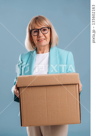 Moving conception, holding box. Senior woman is against background Moving conception, holding box. Senior woman is against background 135602163
