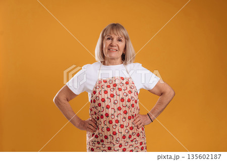 In red apron. Senior housewife is standing against background 135602187