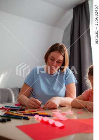 Young kindergarten teacher teaches a girl how to draw postcards for the holiday. Caucasian woman and little girl spend time together. Vertical Young kindergarten teacher teaches a girl how to draw postcards for the holiday. Caucasian woman and little girl spend time together. Vertical 135602467