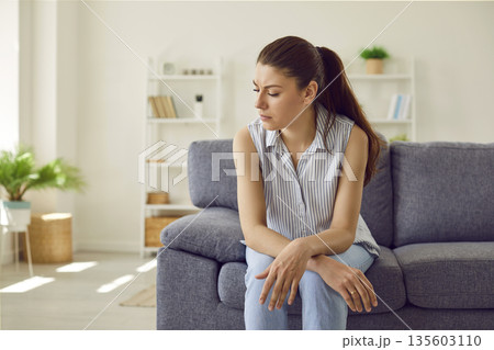Sad upset yound woman sitting alone on the couch in the living room at home. Sad upset yound woman sitting alone on the couch in the living room at home. 135603110