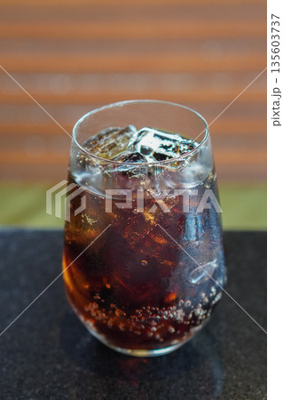 top view cold black drink, ice, in a clear glass, placed on a black marble table, brown wooden wall background, drink, cool, fresh, object, copy space 135603737