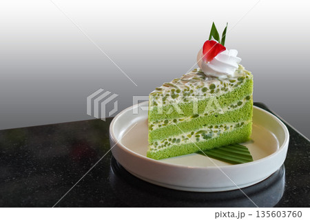 beautiful green and white Singapore Lod Chong Cake. Decorate with whipped cream. and rose petals placed on banana leaves, on a white ceramic plate on black marble floor, white and grey background, 135603760
