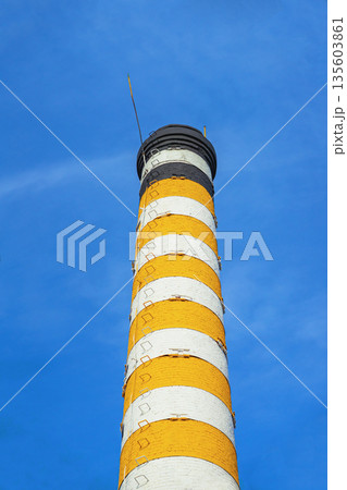 Industrial chimney with yellow bands. Tall industrial chimney with vivid yellow, white stripes against clear blue sky. Industrial chimney with yellow bands. Tall industrial chimney with vivid yellow, white stripes against clear blue sky. 135603861