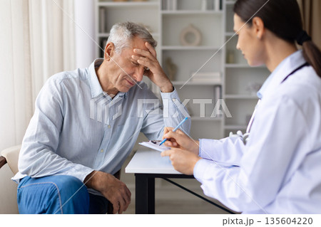 Male patient experiencing headache while doctor records symptoms during consultation in clinic Male patient experiencing headache while doctor records symptoms during consultation in clinic 135604220