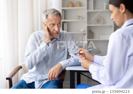 Senior male patient reporting ear pain to female doctor during medical visit 135604223