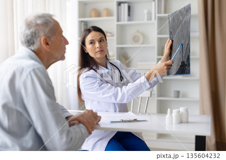 Female doctor holding medical scan and pointing details while consulting male patient 135604232