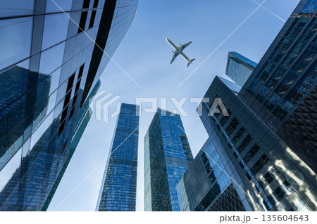 Modern glass skyscrapers on a clear day and passenger jet plane fly over 135604643
