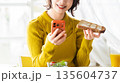 スマートフォンを見ながら食事をする女性 135604737