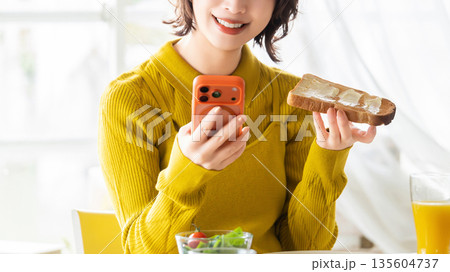 スマートフォンを見ながら食事をする女性 135604737
