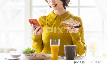スマートフォンを見ながら食事をする女性 スマートフォンを見ながら食事をする女性 135604739