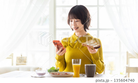 スマートフォンを見ながら食事をする女性 スマートフォンを見ながら食事をする女性 135604740