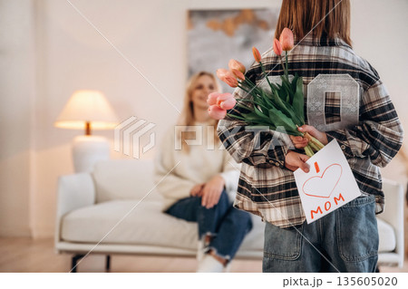 Hiding flowers and gift card for mom. Mother and daughter are together in domestic room Hiding flowers and gift card for mom. Mother and daughter are together in domestic room 135605020