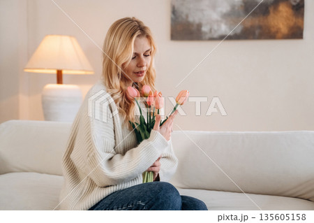 Sitting on the bed. Beautiful young woman is at home with flowers Sitting on the bed. Beautiful young woman is at home with flowers 135605158