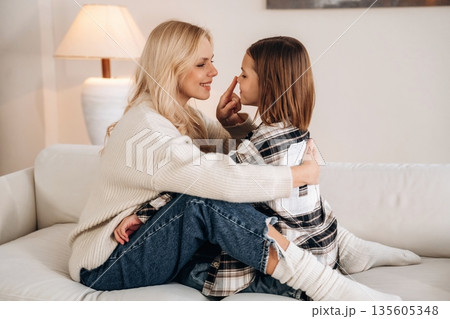 Side view, embracing each other. Mother and daughter are together in domestic room Side view, embracing each other. Mother and daughter are together in domestic room 135605348