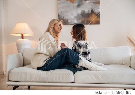 Cozy, sitting on the sofa, side view. Mother and daughter are together in domestic room Cozy, sitting on the sofa, side view. Mother and daughter are together in domestic room 135605369