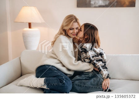 Cozy, sitting on the sofa, side view. Mother and daughter are together in domestic room Cozy, sitting on the sofa, side view. Mother and daughter are together in domestic room 135605372