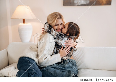 Cozy, sitting on the sofa, side view. Mother and daughter are together in domestic room Cozy, sitting on the sofa, side view. Mother and daughter are together in domestic room 135605375