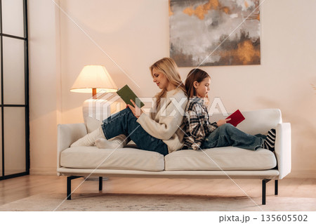 With books, reading time. Mother and daughter are together in domestic room 135605502