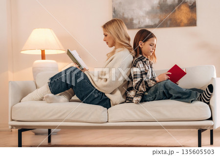 With books, reading time. Mother and daughter are together in domestic room With books, reading time. Mother and daughter are together in domestic room 135605503