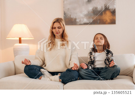 Lotus pose, meditation. Mother and daughter are together in domestic room 135605521