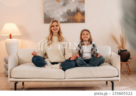 Lotus pose, meditation. Mother and daughter are together in domestic room 135605522