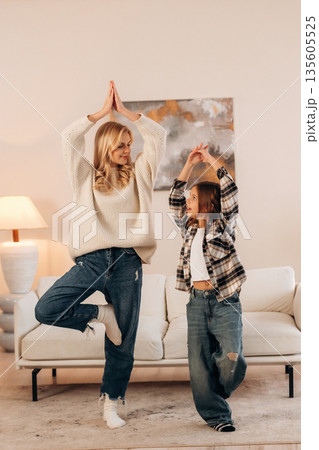 Standing on one leg, sport and yoga. Mother and daughter are together in domestic room Standing on one leg, sport and yoga. Mother and daughter are together in domestic room 135605525