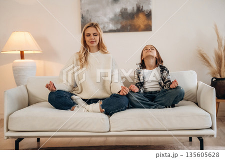 Meditation time, sitting on the sofa. Mother and daughter are together in domestic room 135605628