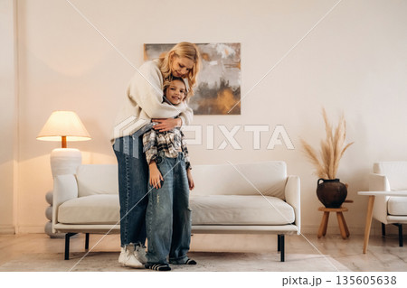 In casual clothes, standing and embracing. Mother and daughter are together in domestic room In casual clothes, standing and embracing. Mother and daughter are together in domestic room 135605638