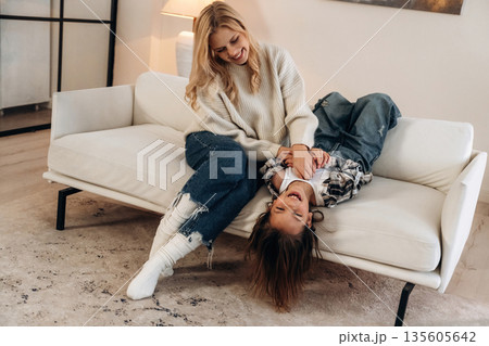 On the sofa, fun, smiling. Mother and daughter are together in domestic room 135605642