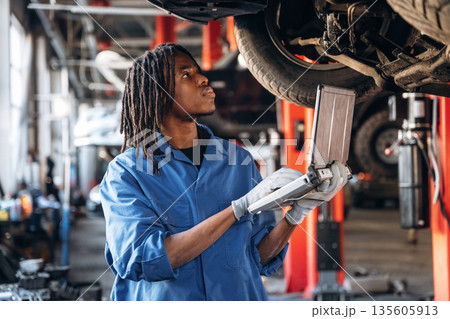 Laptop is in hands. Male mechanic is with car in garage Laptop is in hands. Male mechanic is with car in garage 135605913