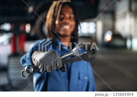 Two wrenches in hand. Male mechanic is with car in garage 135605954