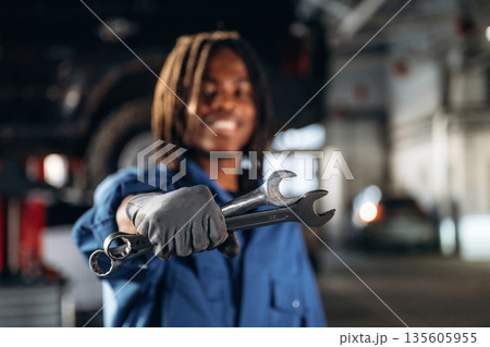 Two wrenches in hand. Male mechanic is with car in garage Two wrenches in hand. Male mechanic is with car in garage 135605955