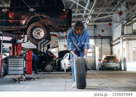 Time to move and change tire. Male mechanic is with car in garage Time to move and change tire. Male mechanic is with car in garage 135605984