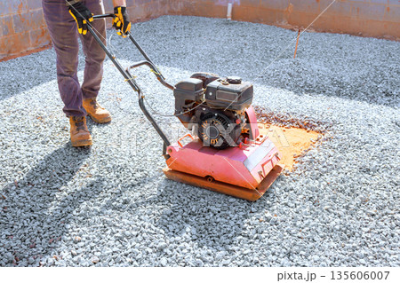 Man operates vibration plate compaction machine on gravel at building site 135606007