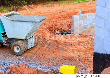 Construction vehicle moves concrete on building site with dirt unfinished wall sections. 135606008