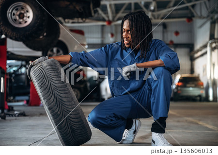 Brand new tire. Male mechanic is with car in garage 135606013