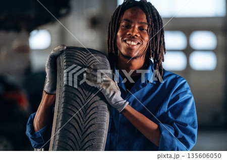 Heavy tire, holding it, changing. Male mechanic is with car in garage Heavy tire, holding it, changing. Male mechanic is with car in garage 135606050