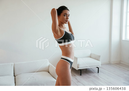 Black clothes with white edges. Young woman with slim body type is indoors Black clothes with white edges. Young woman with slim body type is indoors 135606438